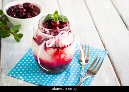 Sweet cherry cheesecake in a mason jar on wooden table Stock Photo