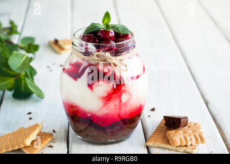 Sweet cherry cheesecake in a mason jar on wooden table Stock Photo