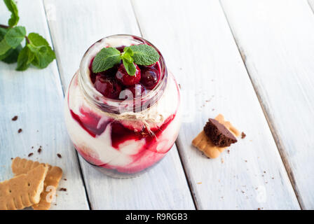 Sweet cherry cheesecake in a mason jar on wooden table Stock Photo