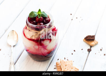 Sweet cherry cheesecake in a mason jar on wooden table Stock Photo