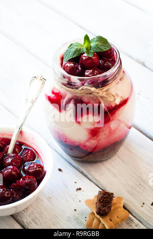 Sweet cherry cheesecake in a mason jar on wooden table Stock Photo