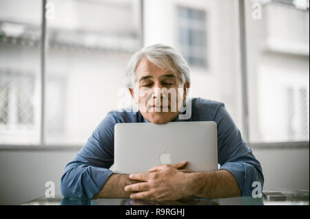 Content mature businessman hugging his laptop computer. Stock Photo