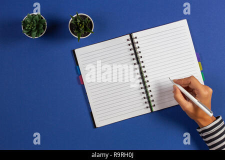 Girl hand writing with pen in diary notebook over blue background. Stock Photo