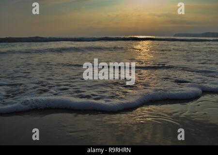 A line of foaming bubbles on a sandy beach at England's south coast, the famous white cliffs in silhouette as the sun sets and is reflected off the ca Stock Photo