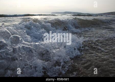 Violent and explosive bubbling of small waves on the sandy beaches of south England. Larger waves roll in the background, and the famous chalk cliffs  Stock Photo