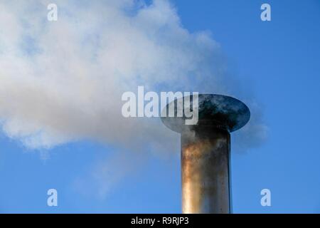 Smoke billows from the vent pipe of a stainless steel outdoor furnace. Stock Photo