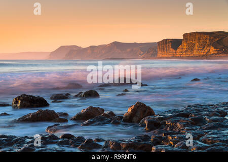 Burton Bradstock, Dorset, UK.  27th December 2018. UK Weather.  View west from the beach at Burton Bradstock on the Dorset Jurassic Coast looking towards West Bay and Golden Cap at sunset.  Picture Credit: Graham Hunt/Alamy Live News Stock Photo