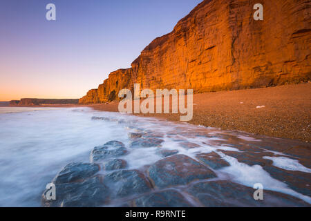 Burton Bradstock, Dorset, UK.  27th December 2018. UK Weather.  The sandstone cliffs at the beach at Burton Bradstock on the Dorset Jurassic Coast glow orange at sunset after an afternoon of clear sunny skies.  Picture Credit: Graham Hunt/Alamy Live News Stock Photo