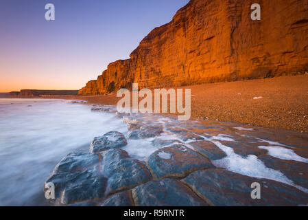 Burton Bradstock, Dorset, UK.  27th December 2018. UK Weather.  The sandstone cliffs at the beach at Burton Bradstock on the Dorset Jurassic Coast glow orange at sunset after an afternoon of clear sunny skies.  Picture Credit: Graham Hunt/Alamy Live News Stock Photo