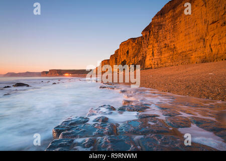 Burton Bradstock, Dorset, UK.  27th December 2018. UK Weather.  The sandstone cliffs at the beach at Burton Bradstock on the Dorset Jurassic Coast glow orange at sunset after an afternoon of clear sunny skies.  Picture Credit: Graham Hunt/Alamy Live News Stock Photo