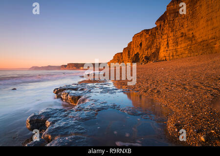 Burton Bradstock, Dorset, UK.  27th December 2018. UK Weather.  The sandstone cliffs at the beach at Burton Bradstock on the Dorset Jurassic Coast glow orange at sunset after an afternoon of clear sunny skies.  Picture Credit: Graham Hunt/Alamy Live News Stock Photo