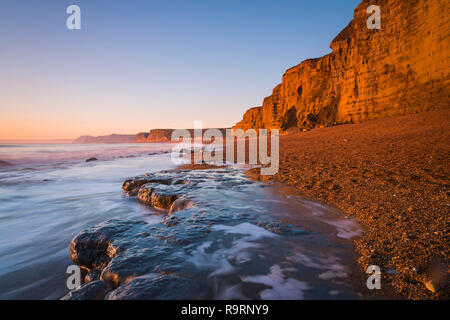 Burton Bradstock, Dorset, UK.  27th December 2018. UK Weather.  The sandstone cliffs at the beach at Burton Bradstock on the Dorset Jurassic Coast glow orange at sunset after an afternoon of clear sunny skies.  Picture Credit: Graham Hunt/Alamy Live News Stock Photo