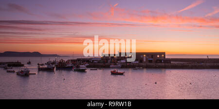 Lyme Regis, Dorset, UK. 28th Dec, 2018. UK Weather: The sky glows orange over the historic Cobb at sunrise as Lyme Regis enjoys a chilly and bright winter's morning. Credit: Celia McMahon/Alamy Live News Stock Photo