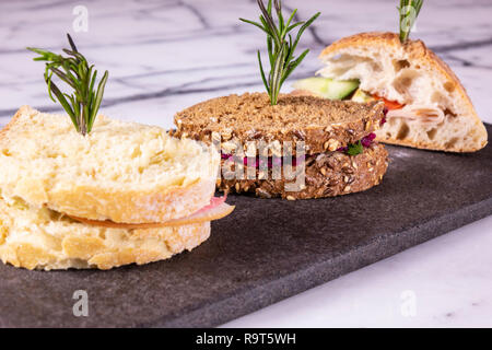 Three sandwiches with salad, ham, cheese and tomatoes on marble table. Stock Photo