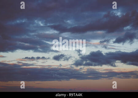 Evening sky scene with golden light from the setting sun and blue-tinting filled with cloud streaks, dark blue background Stock Photo