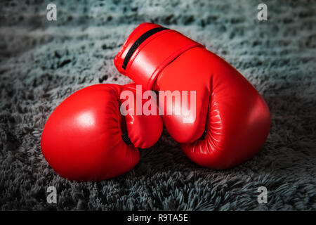 Red boxing gloves lie on the floor on grey carpet on dark background Stock Photo