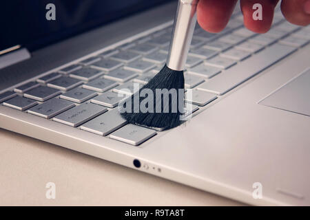 Cleaning keyboard from dust by black brush. Cleaning concept. Selective focus. cleaning the keyboard of the modern gray ultrabook transformer with a b Stock Photo