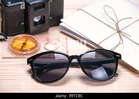 Sunglasses, compass, vintage film camera and a bunch of old letters on a light wooden background. Abstract of summer travels. Stock Photo