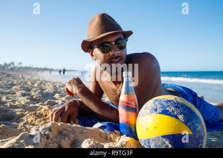 Tourist man laying in the sand sunbathing on the beach in the Caribbean, Tourist wearing sunshades and hat Stock Photo