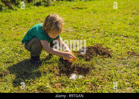 The boy plays recycling. He buries plastic disposable dishes and biodegradable dishes Stock Photo