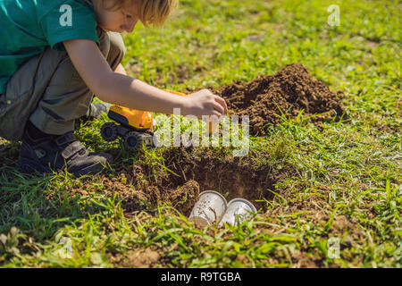 The boy plays recycling. He buries plastic disposable dishes and biodegradable dishes Stock Photo