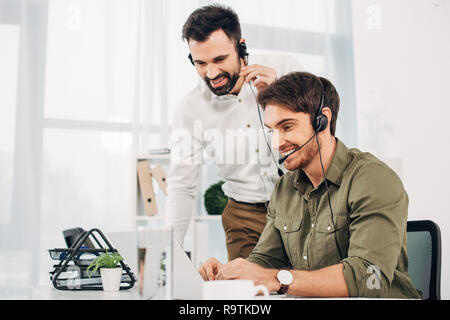smiling call center operators looking at laptop screen in office Stock Photo