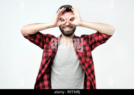 Hispanic handsome man showing hero or owl sign or like wearing glasses for better eyesight. Studio shoot. Stock Photo