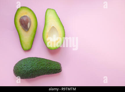 Ripe organic avocados with seed, avocado half and whole fruit on pink background with copyspace. Stock Photo