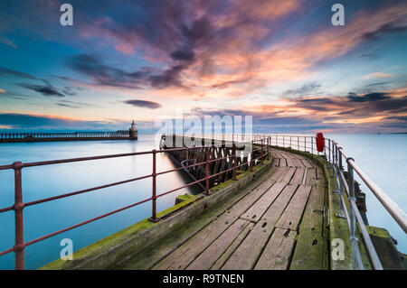 A colourful sunrise on a cold winter morning at Blyth Pier Northumberland, looking towards the lighthouse & lonesome fisherman at the end of the pier Stock Photo