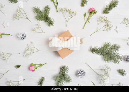 Abstract Christmas background decorated with gift in center and xmas elements - cones, tree branches, roses on a white wooden background Stock Photo