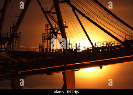 Crane at Felixstowe docks silhouetted by rising moon behind red background Stock Photo