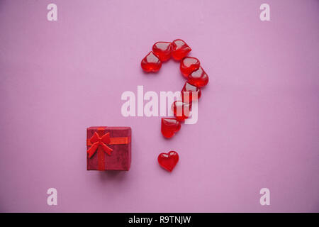A box with a gift and a number of question marks laid out from small red hearts. Concept for Valentine's Day or another love event. A question mark me Stock Photo