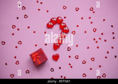 A box with a gift and a number of question marks laid out from small red hearts. Concept for Valentine's Day or another love event. A question mark me Stock Photo