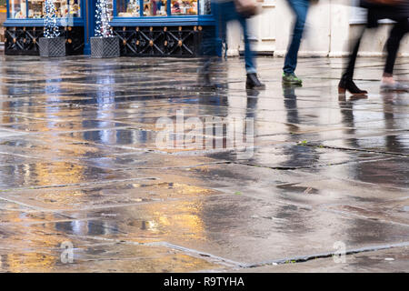Christmas shoppers walking on a rain soaked pavement in Bath at dusk. Stock Photo