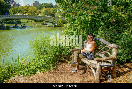 Young Artistic woman siting on the wooden bench by the lake in New York Central park Stock Photo