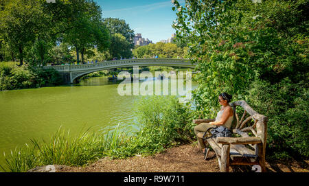 Young Artistic woman siting on the wooden bench by the lake in New York Central park Stock Photo