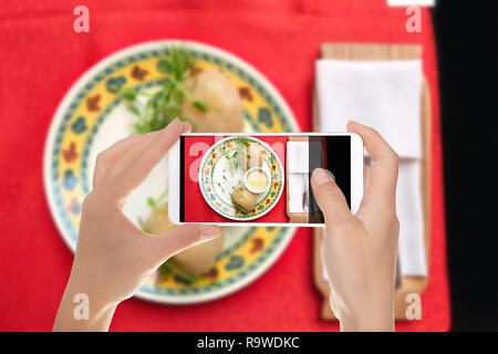 A man is a making photo of traditional Lithuanian dishes from potatoes - zeppelins with sauce on a plate on a mobile phone Stock Photo