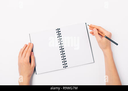 Flat lay woman's hands holding pencil near open blank notebook on clean white table, view from above. Stock Photo