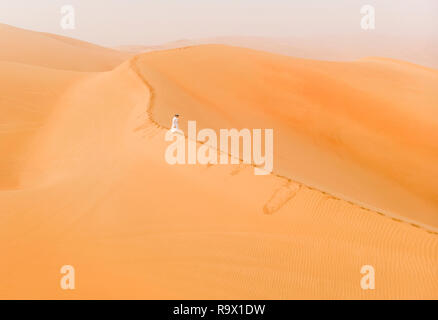 man in traditional emirati outfit walking in massive sand dunes of Liwa desert Stock Photo