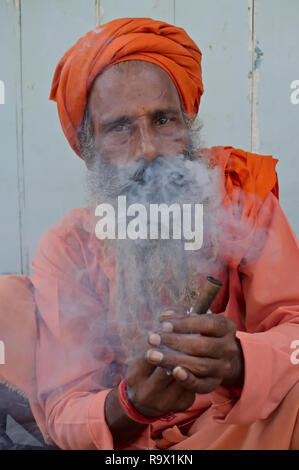 A sadhu or holy man in Mumbai, India, sqatting by the roadside smoking hashish, locally called charas, in imitation of his favority deity Shiva Stock Photo