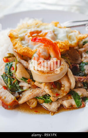 Rice topped with stir-fried pork, squid, shrimp, chicken, crispy pork and basil and fried egg. Stock Photo
