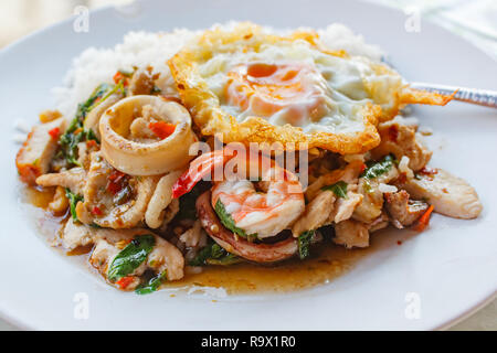 Rice topped with stir-fried pork, squid, shrimp, chicken, crispy pork and basil and fried egg. Stock Photo