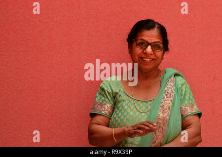 Happy looking senior Indian lady wearing traditional suit and spectacles standing against a pink wall in pink city Jaipur, Rajasthan, India Stock Photo