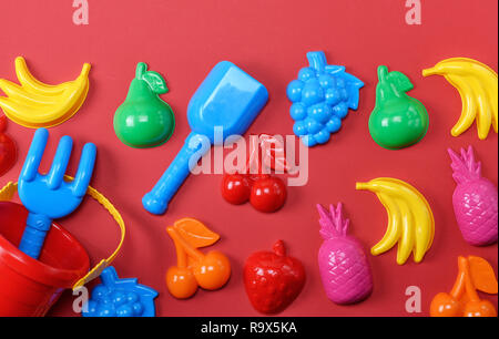 plastic childrens toys in the form of fruit and a bucket on a red background Stock Photo