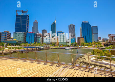 Perth, Western Australia - Jan 3, 2018: skyscrapers of Central Business District seen from wooden walkway of arched pedestrian bridge of Elizabeth Quay on Swan River. Blue sky, copy space. Stock Photo