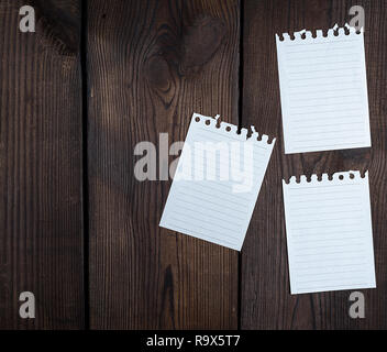 empty white sheets in a line torn out of notepad on a brown wooden background, copy space Stock Photo