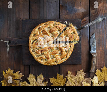 baked whole round apple pie on a rectangular old brown cutting board , top view Stock Photo