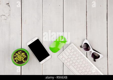 Wireless slim white keyboard and green mouse, smartphone, glasses, flower on white wooden background Stock Photo