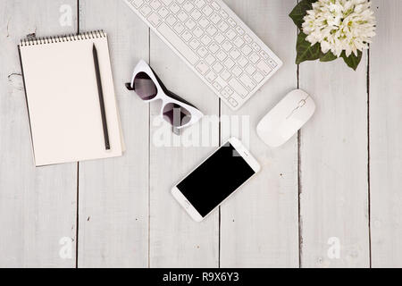 Wireless slim keyboard and mouse, smartphone, notepad, glasses, flower on white wooden background Stock Photo