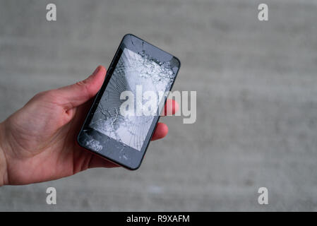 Hand holding phone with broken screen by hammer Stock Photo